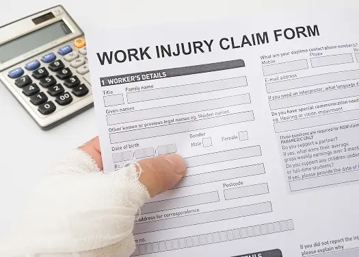 Injured worker's hand filling out a work injury claim form.