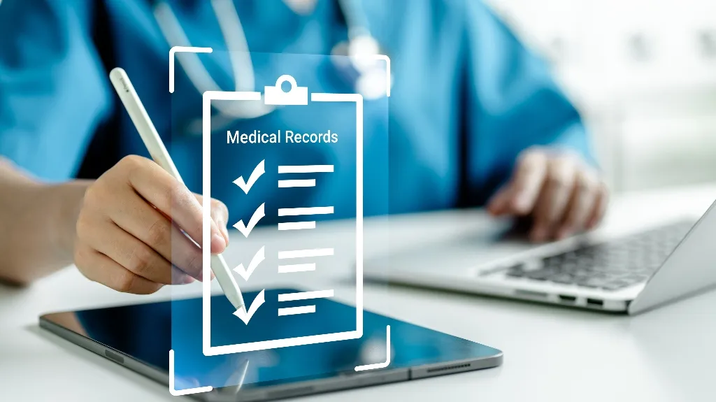 Person in medical scrubs using stylus on tablet with digital medical records display.