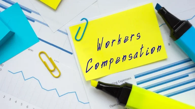 Yellow sticky note with "Workers Compensation" text, blue and yellow paperclips, highlighters, and financial charts.