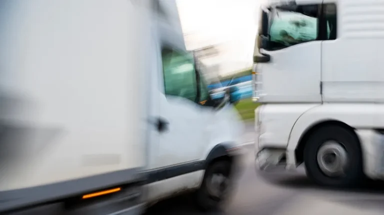 Blurred image of two white trucks moving in opposite directions on a road.
