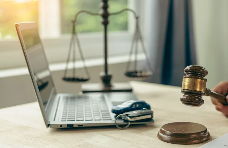 Wooden gavel striking block beside laptop and scales of justice on desk.