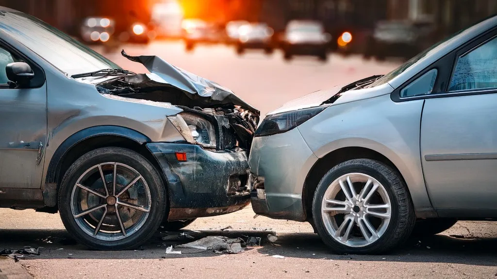 Two silver cars with front-end damage after a collision on a city street.