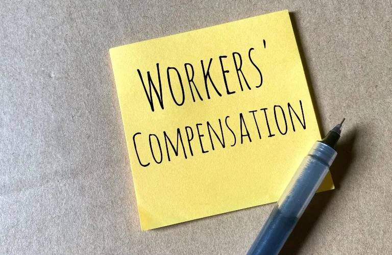 Yellow sticky note with "WORKERS' COMPENSATION" text written in black ink, accompanied by a pen.