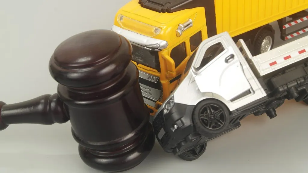 Dark wooden gavel positioned next to yellow and white toy trucks on a neutral background.