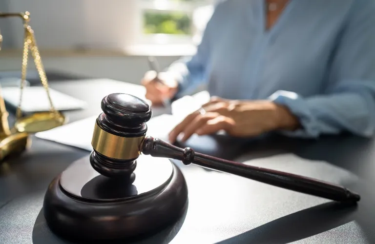 Dark wooden judge gavel and base on desk with blurred person writing in background.